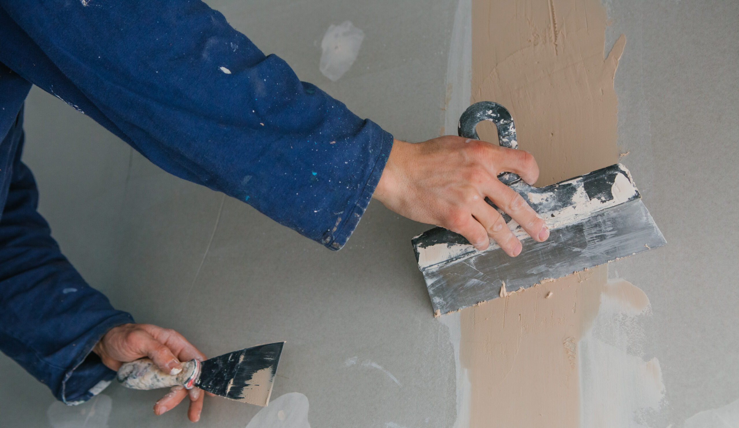 plasterer man works plastering two trowels on plasterboard in blue uniform